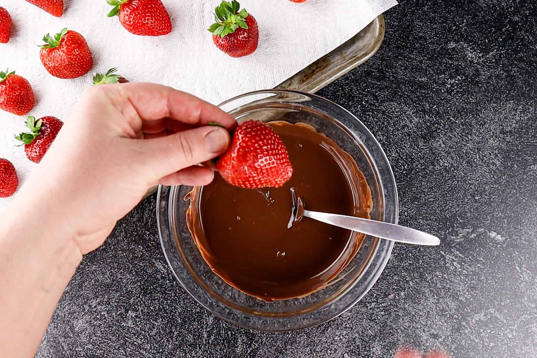 holding a strawberry by the green leaves at the top