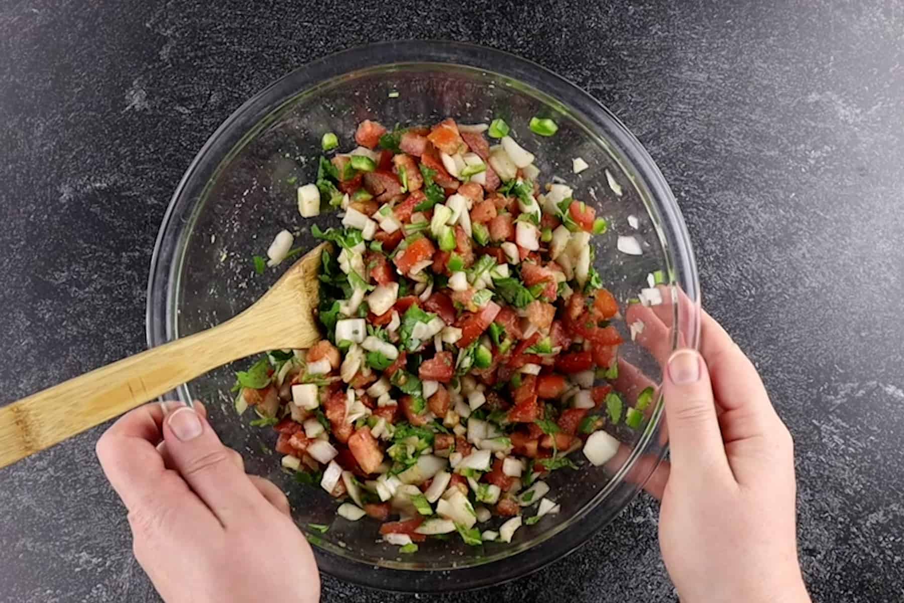 mixing pico together with a wooden spoon in clear glass bowl.