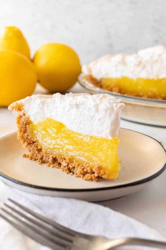 slice of lemon meringue pie with lemons and pie in the background