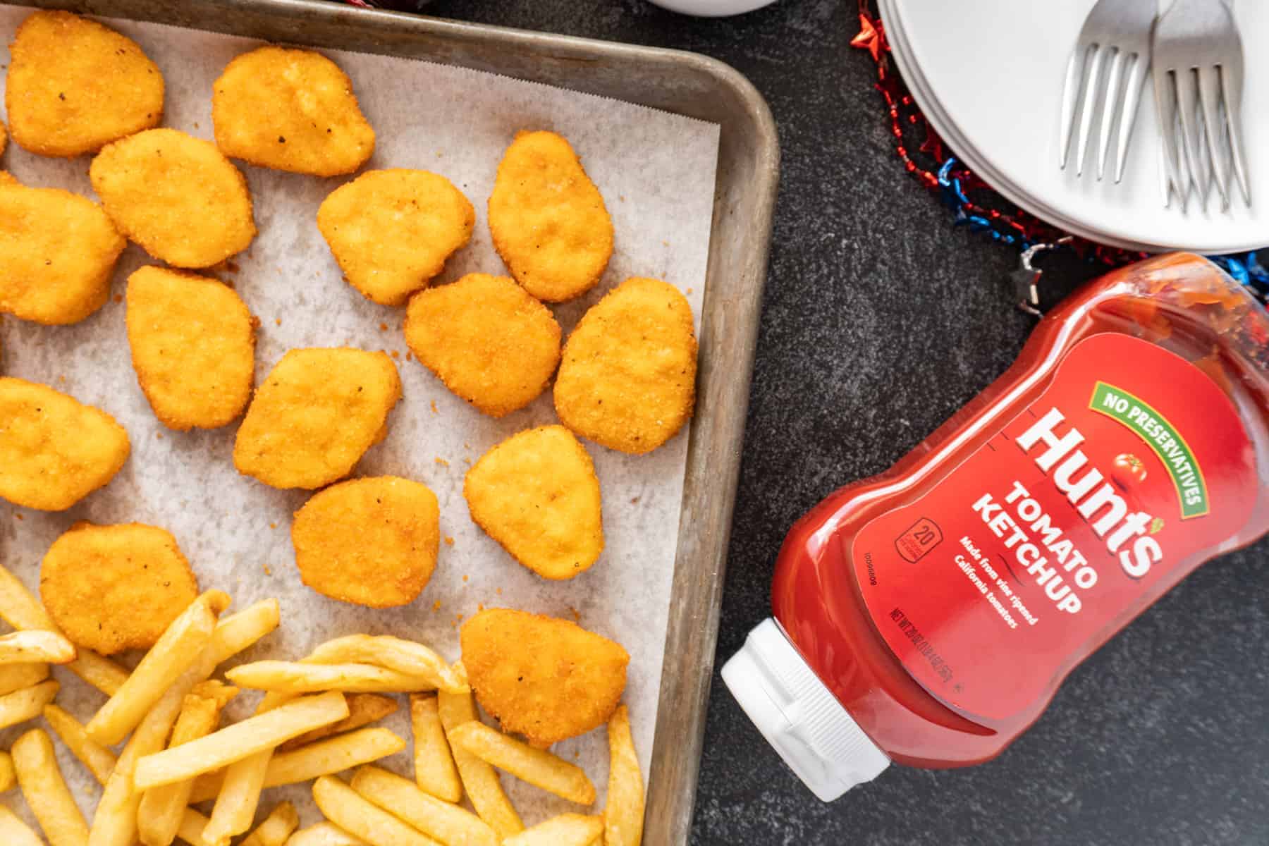 chicken nuggets and fries on baking sheet with bottle of ketchup next to it