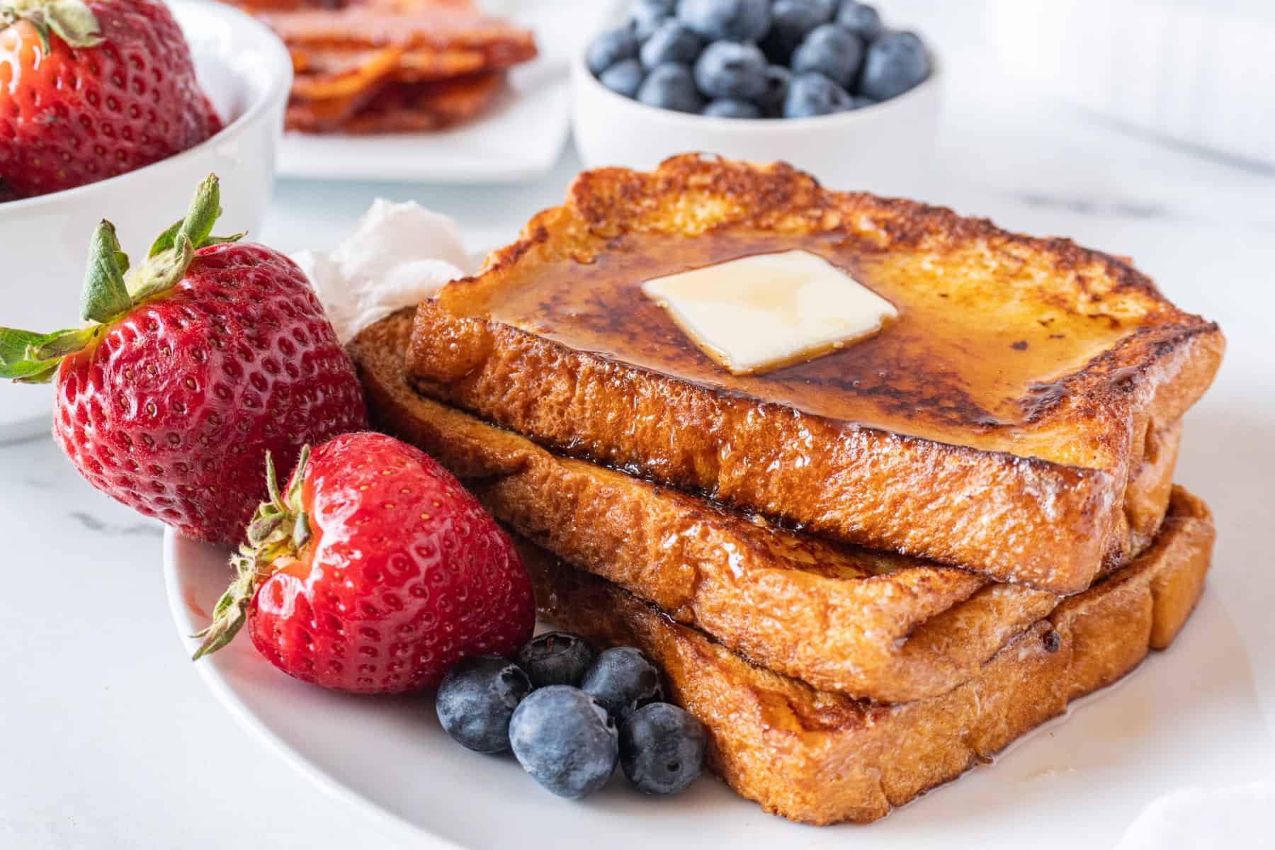 stack of french toast with butter and berries and syrup on a plate horizontal image