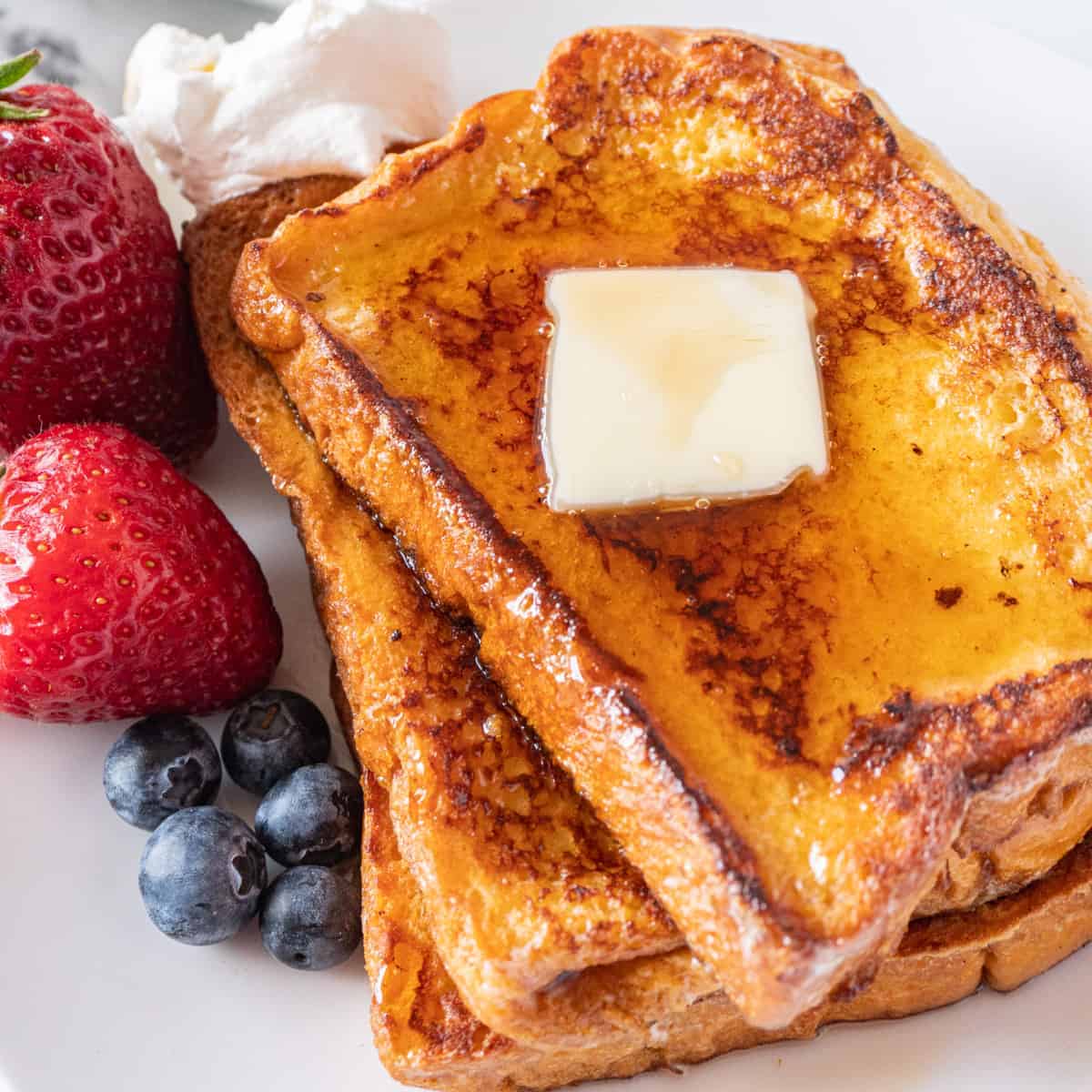 featured french toast image- french toast with butter and berries and syrup on a plate