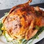 herb butter turkey with golden skin on what platter surrounded by fresh herbs and lemon slices.