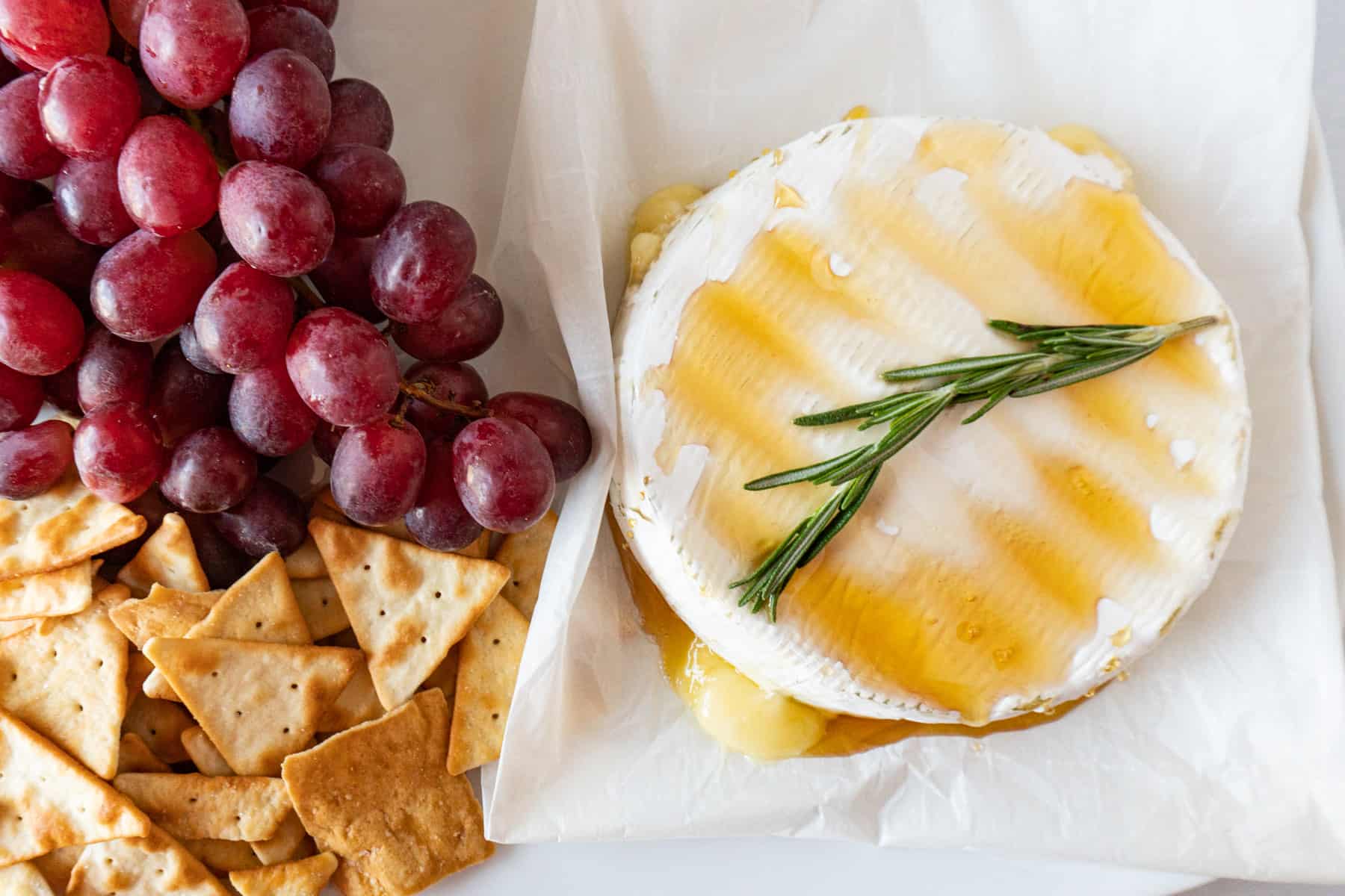 brie with honey and rosemary next to crackers and grapes