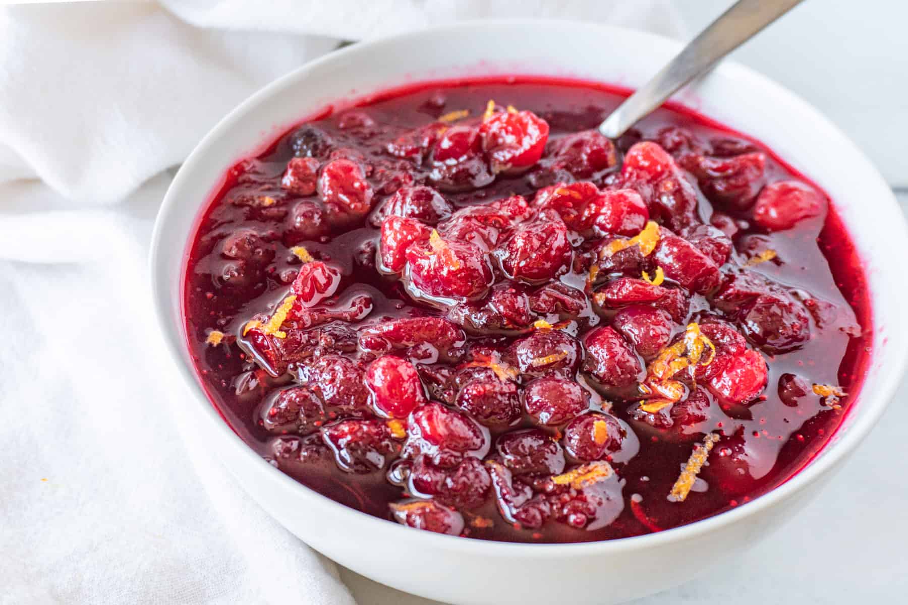Cranberry sauce in a white bowl with a spoon sticking out.