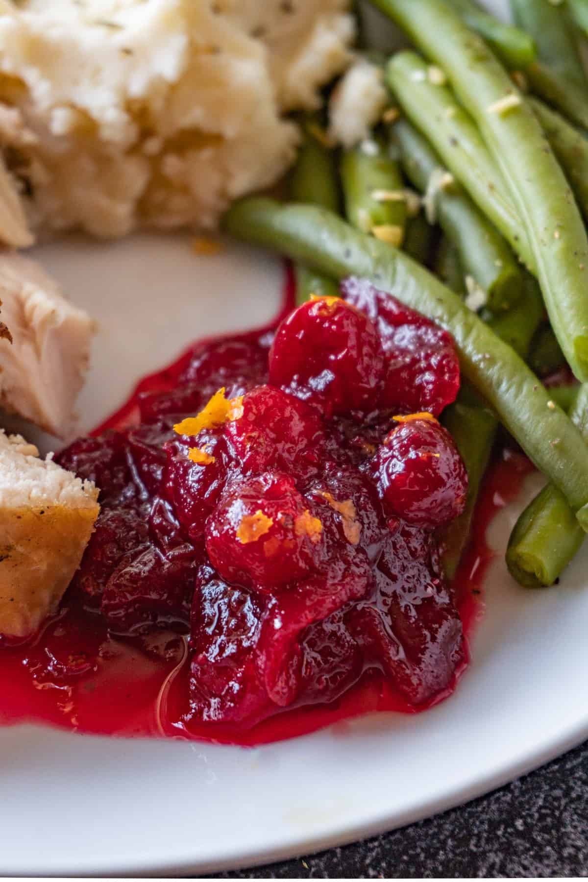 cranberry sauce on plate with green beans, turkey, and mashed potatoes