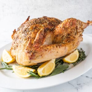 baked turkey on platter with lemon and sage leaves around it featured image