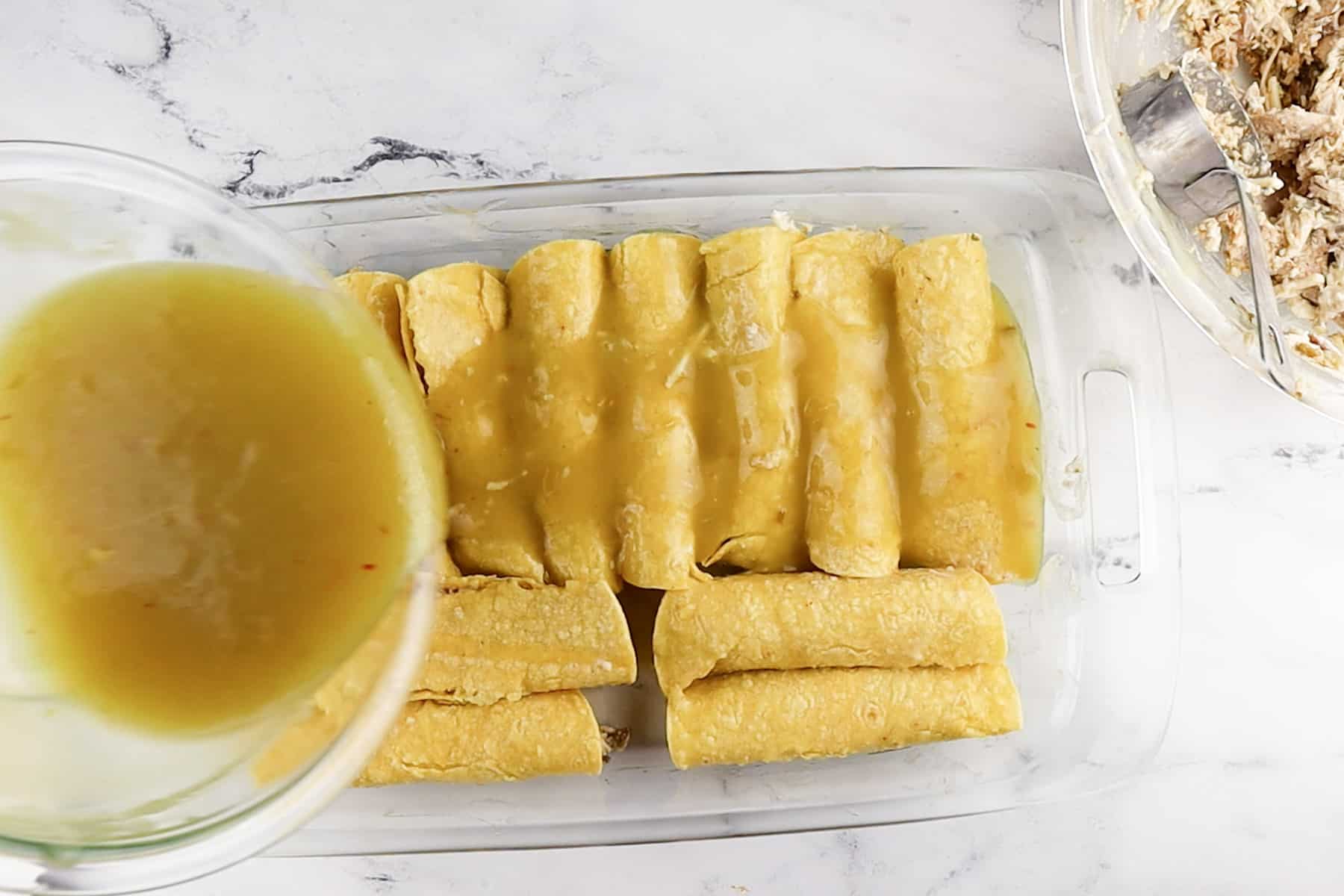 pouring leftover enchilada souce over rolled enchilads