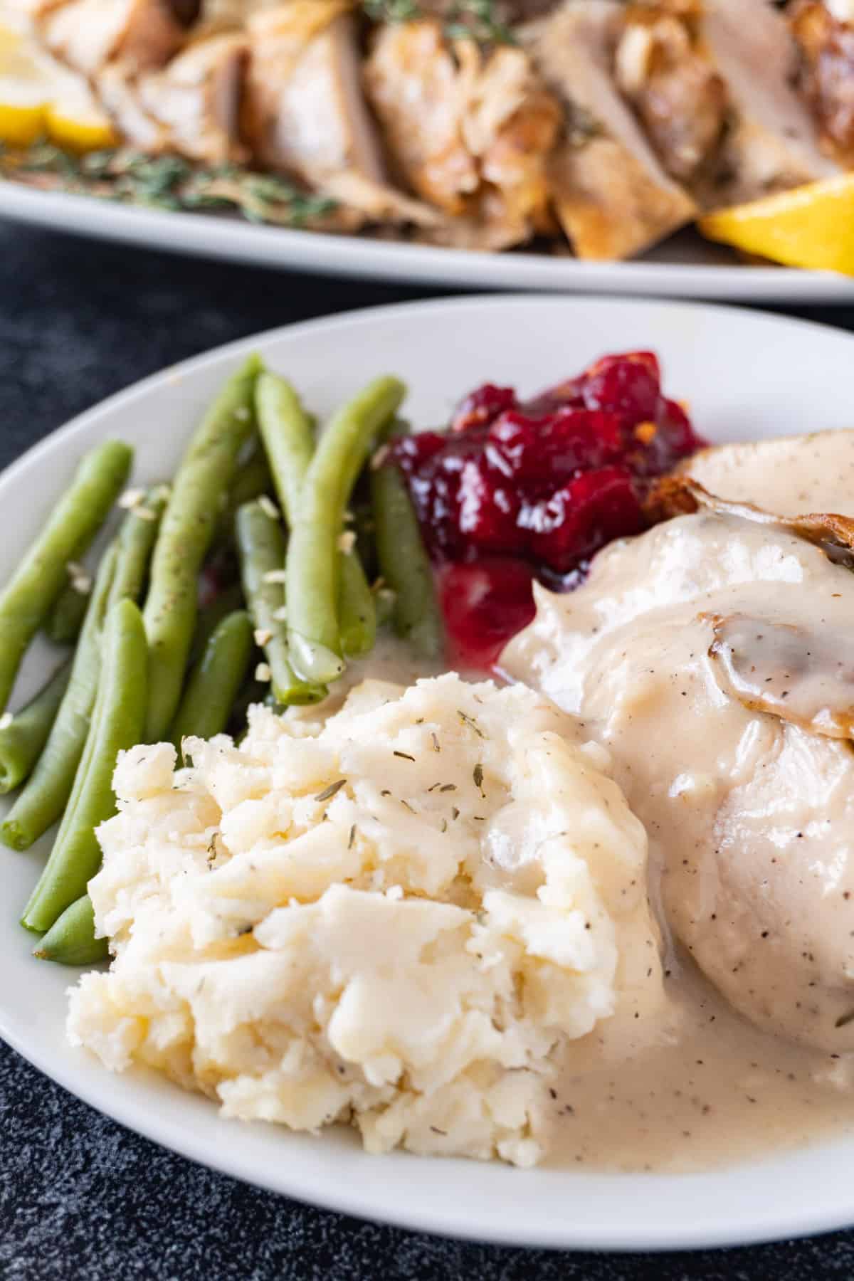 mashed potatoes with gravy on plate with green beans turkey and cranberry sauce