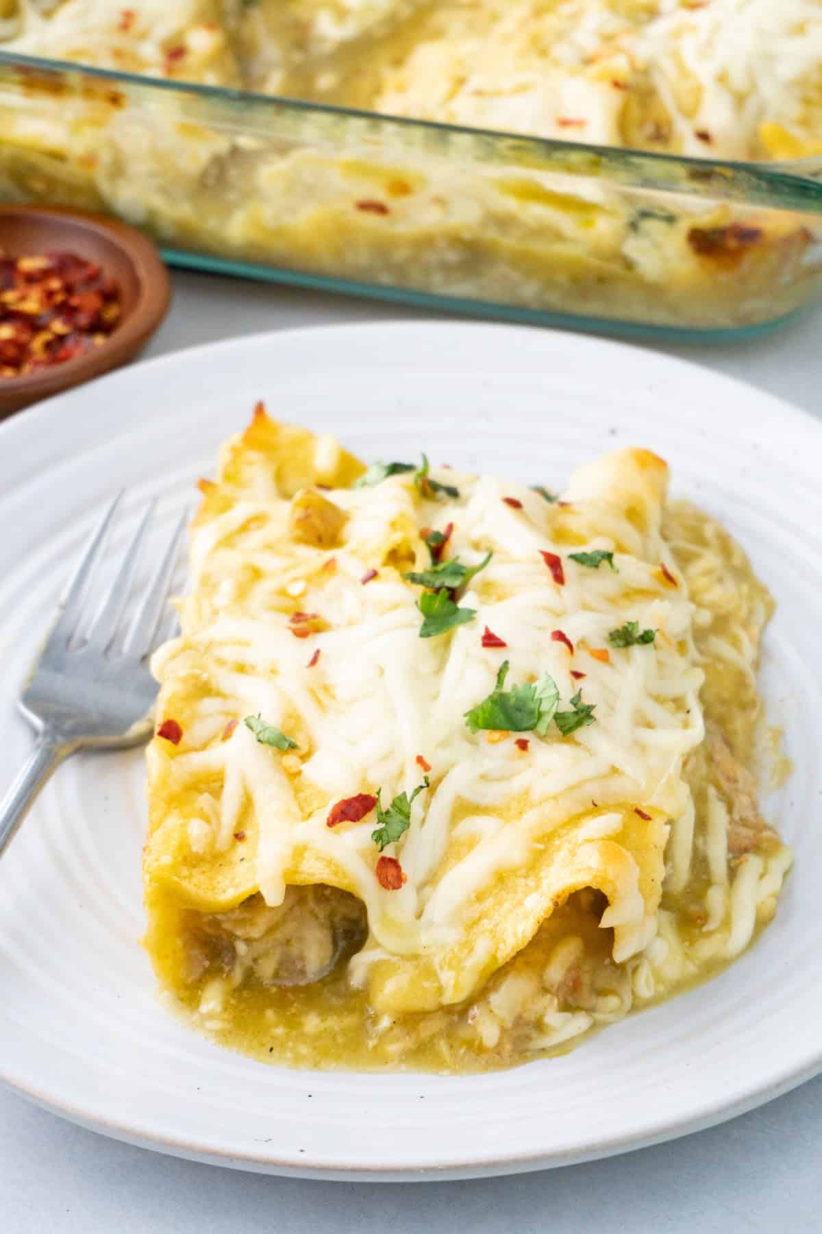 green chile chicken enchiladas on a white plate with a fork next to it.