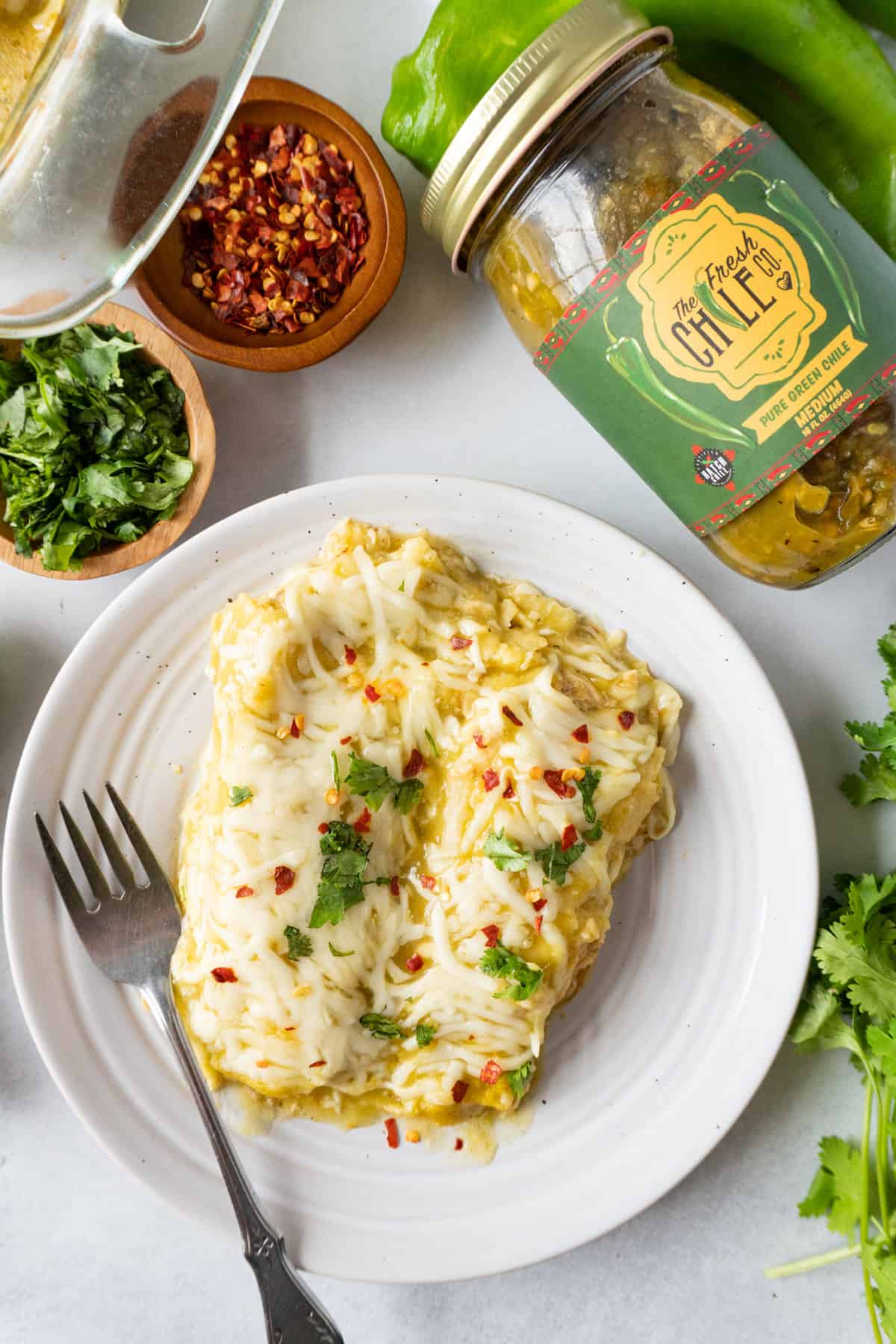 flat lay of enchilada on plate with green chile jar, and spices next to plate