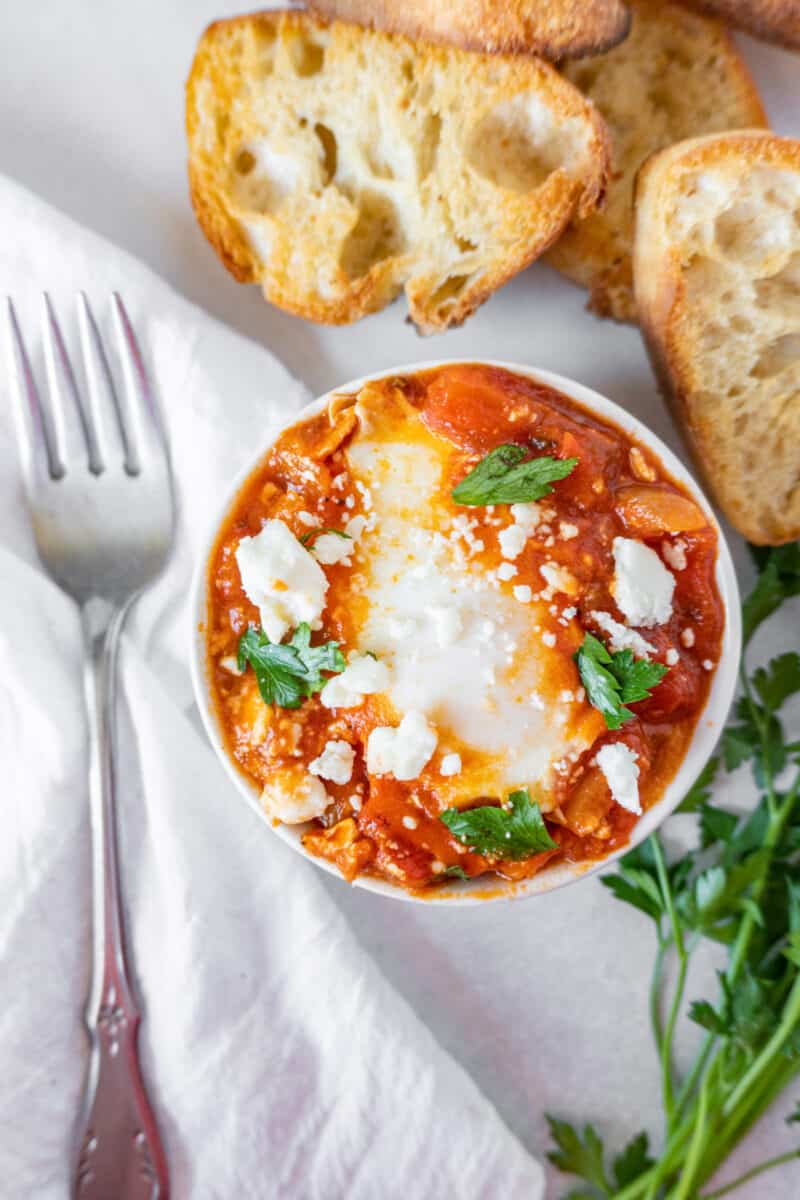 close up of shakshuka in white bowl with toasted bread