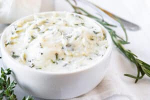 garlic herb butter in white bowl with rosemary spring near