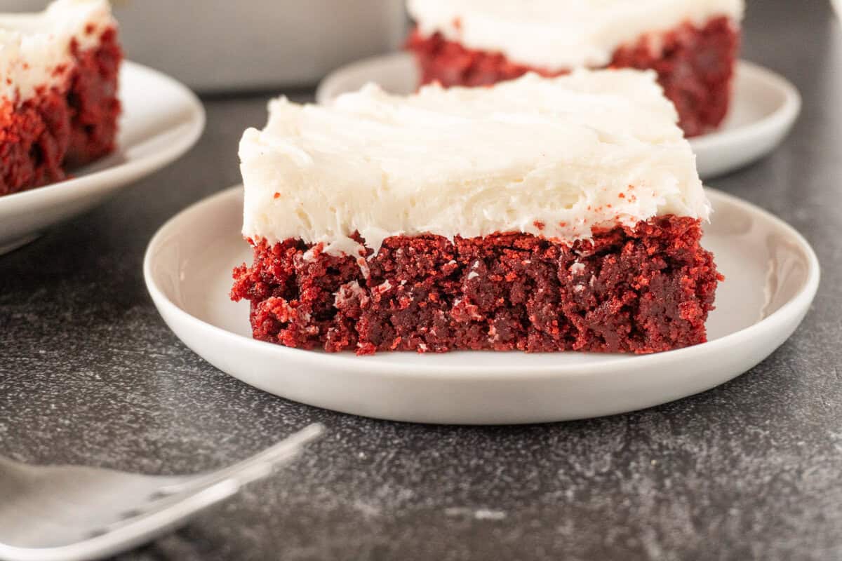 red velvet brownie with cream cheese frosting on white plate.