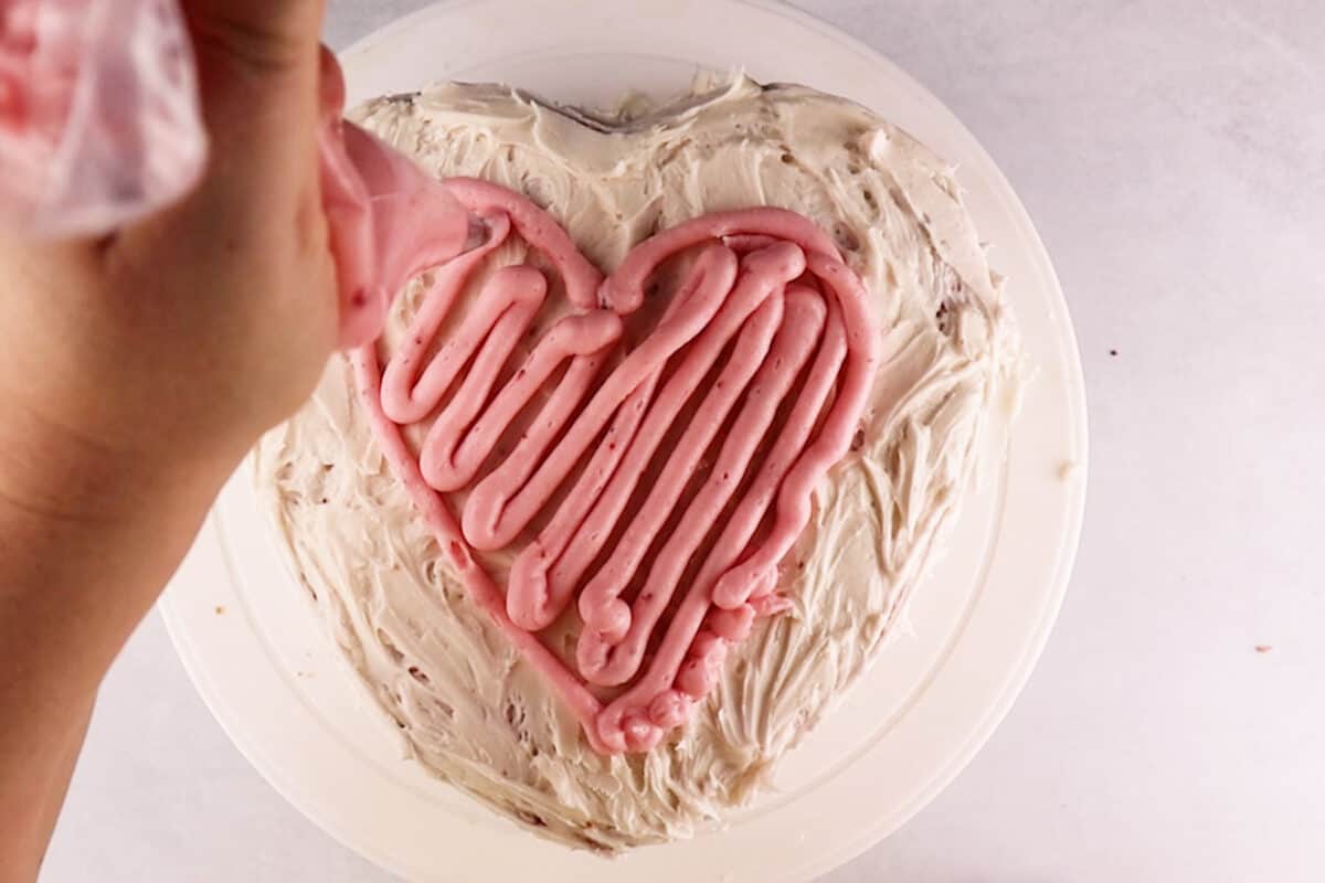 piping heat on top of cake with pink frosting