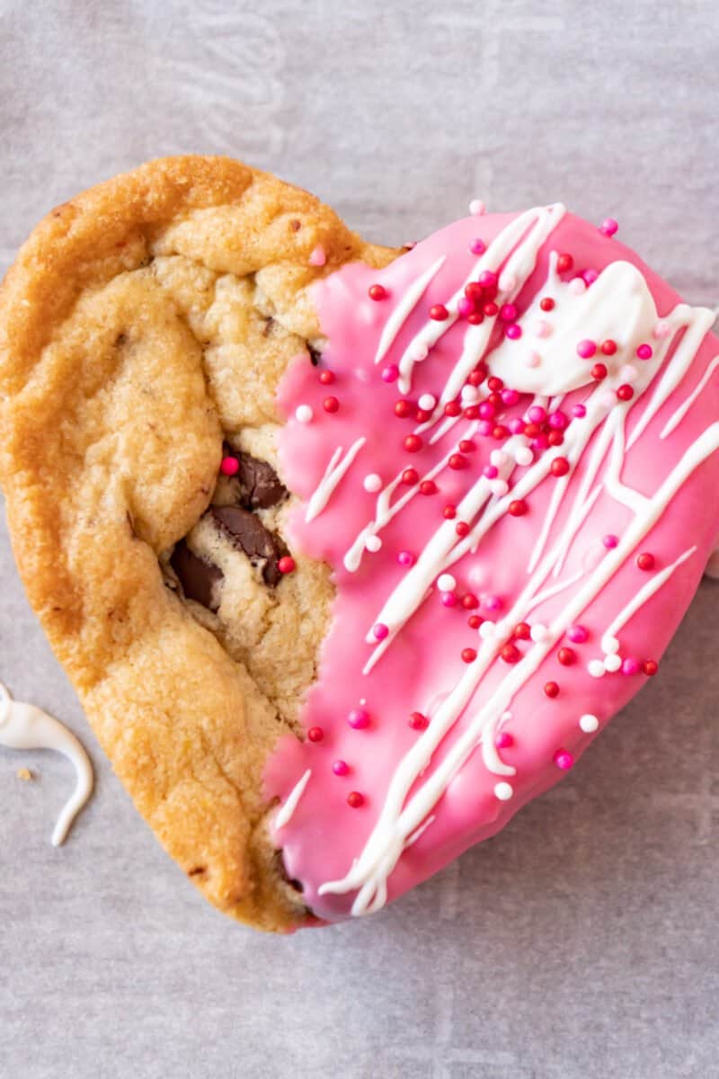 heart shaped chocolate chip cookie half pink with sprinkles and white strips
