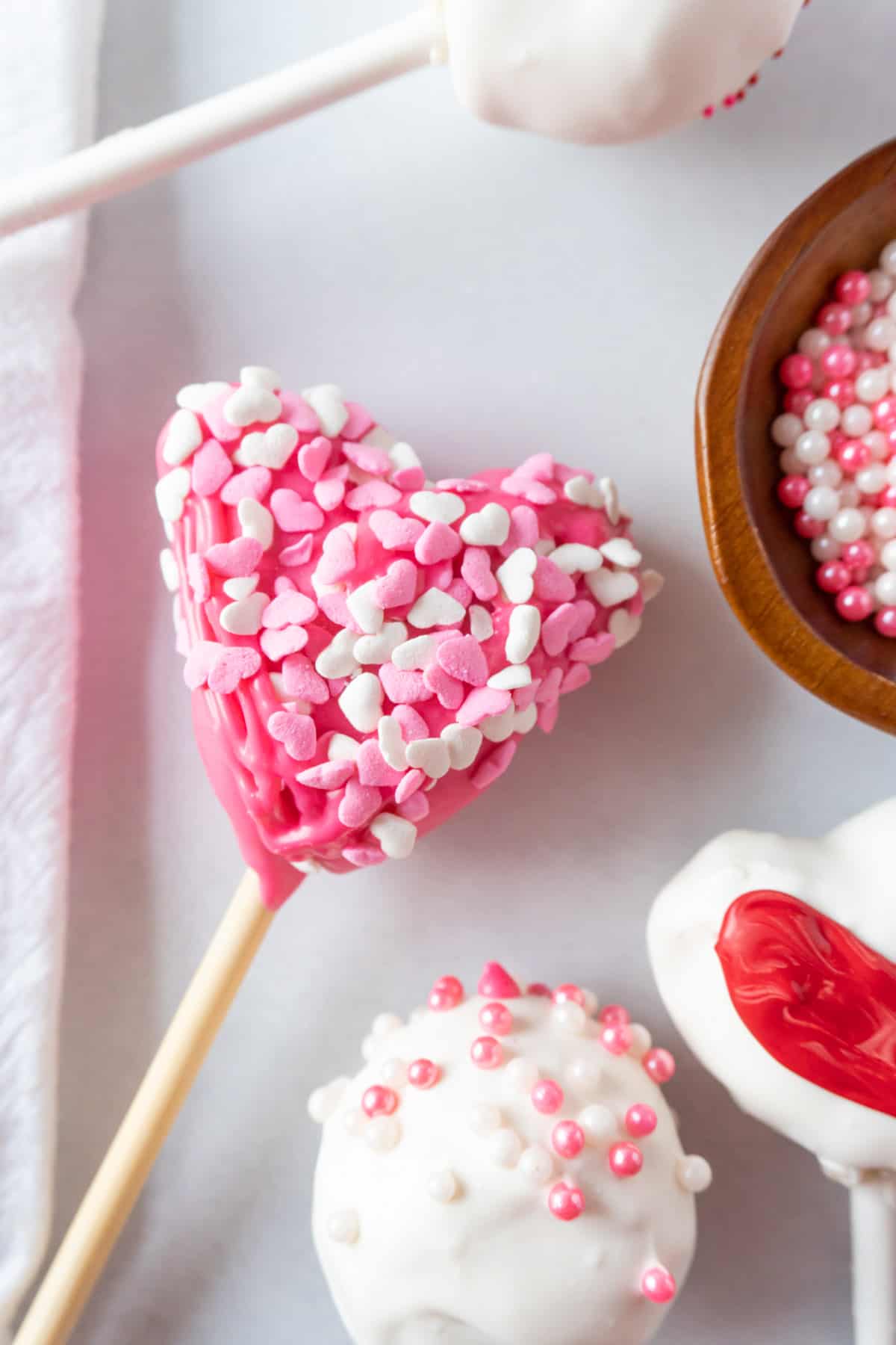 pink heart cake pop with heart sprinkles and white cake pop with pink and white sprinkles.