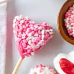 Pink heart-shaped cake pop covered in heart sprinkles.