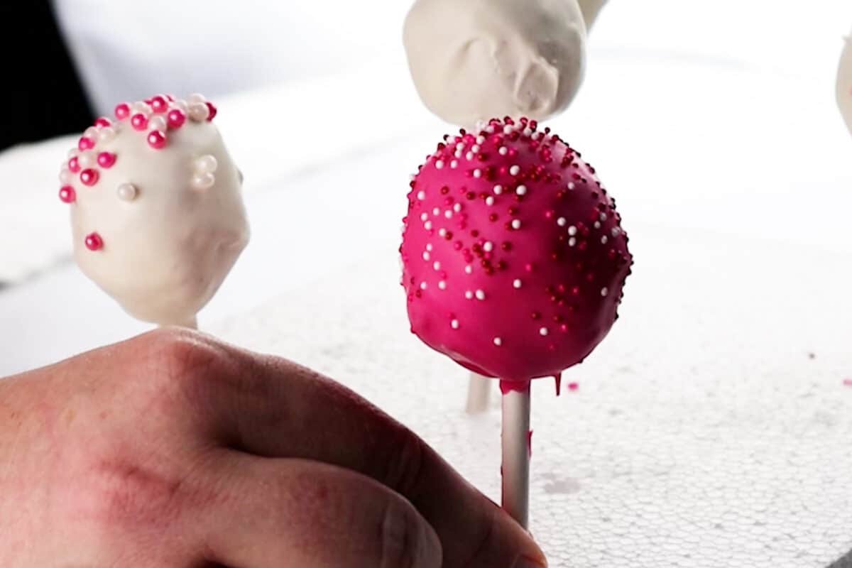 placing dipped cake pop into Styrofoam to strand up