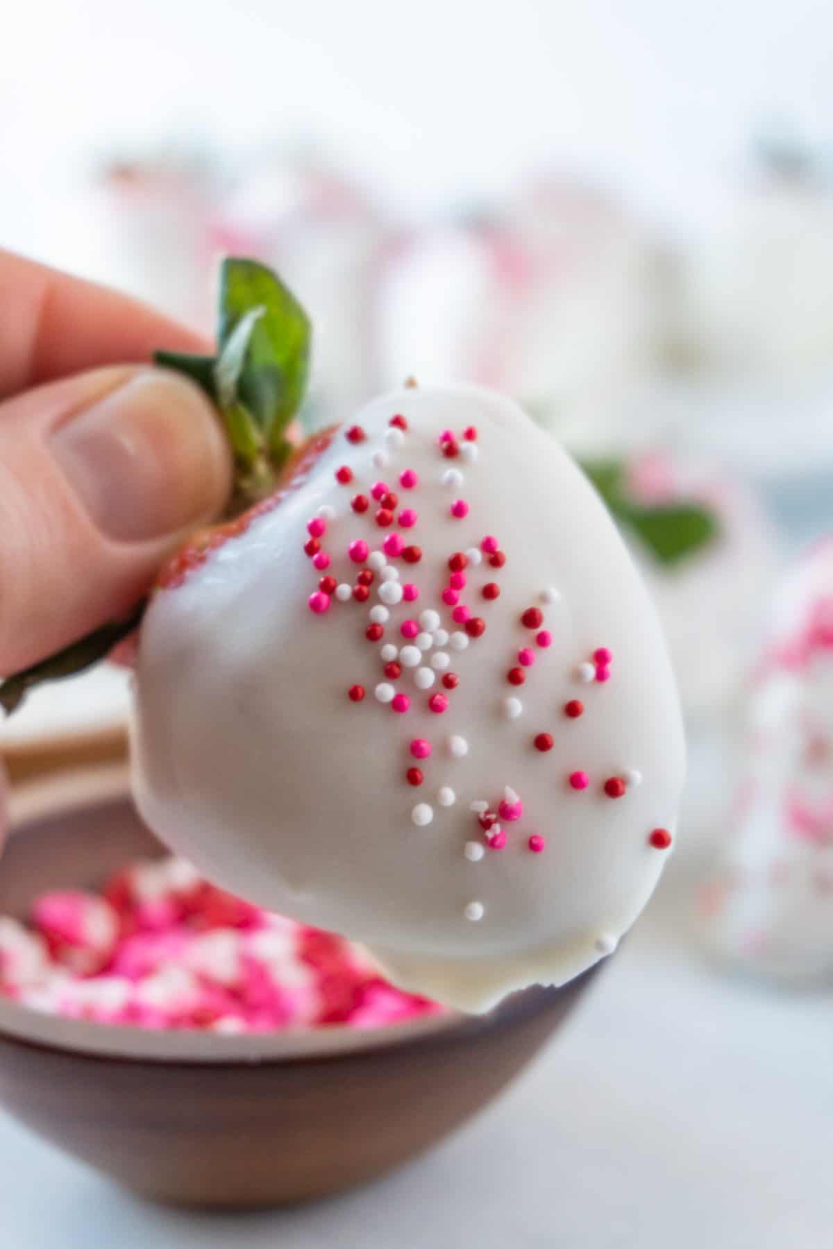 holding a white chocolate dipped strawberry with pink sprinkles.