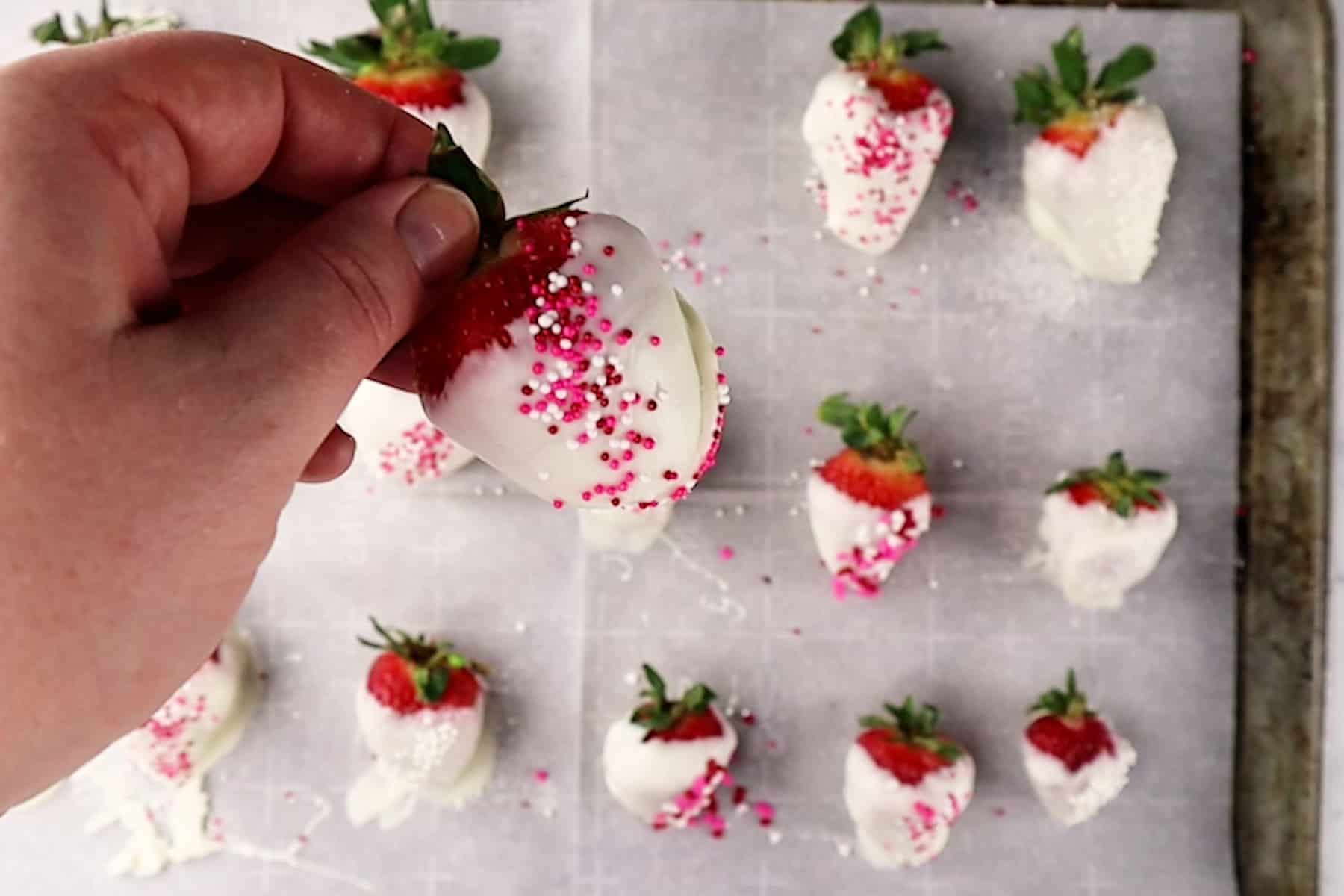 holding a dipped strawberry over a tray of already dipped and decorated strawberries.