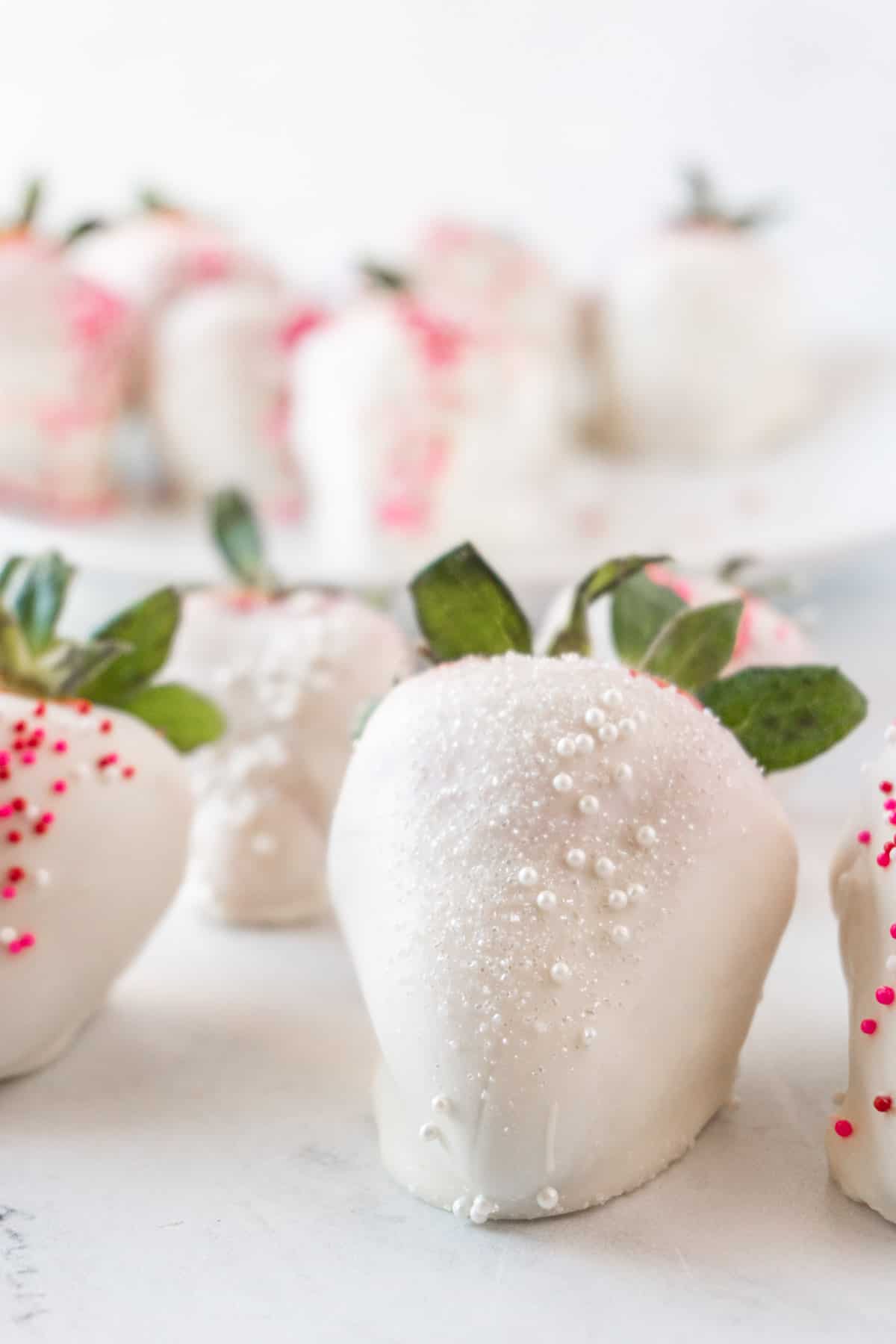 white chocolate strawberry with white sprinkles on marble counter top.