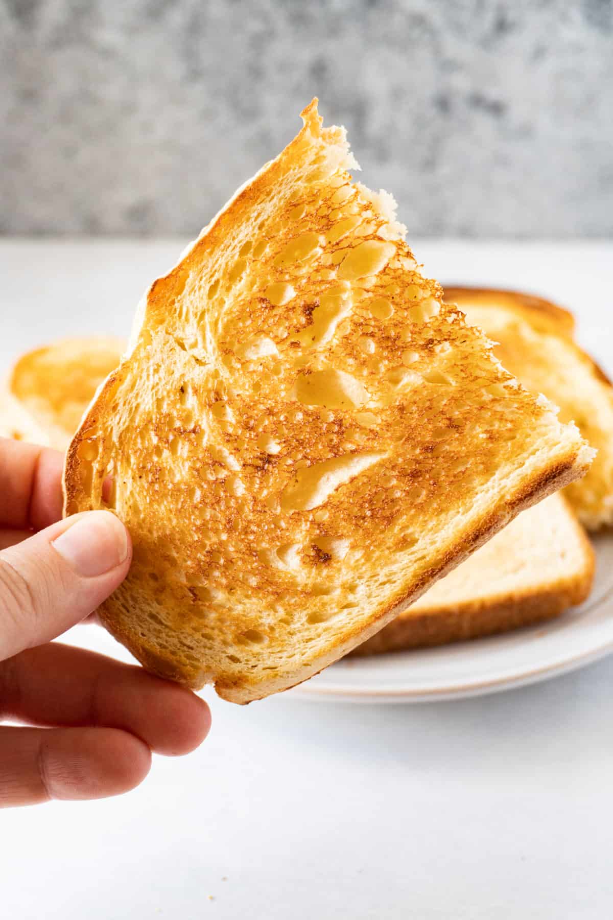 holding a piece of toasted bread from the oven in hand.