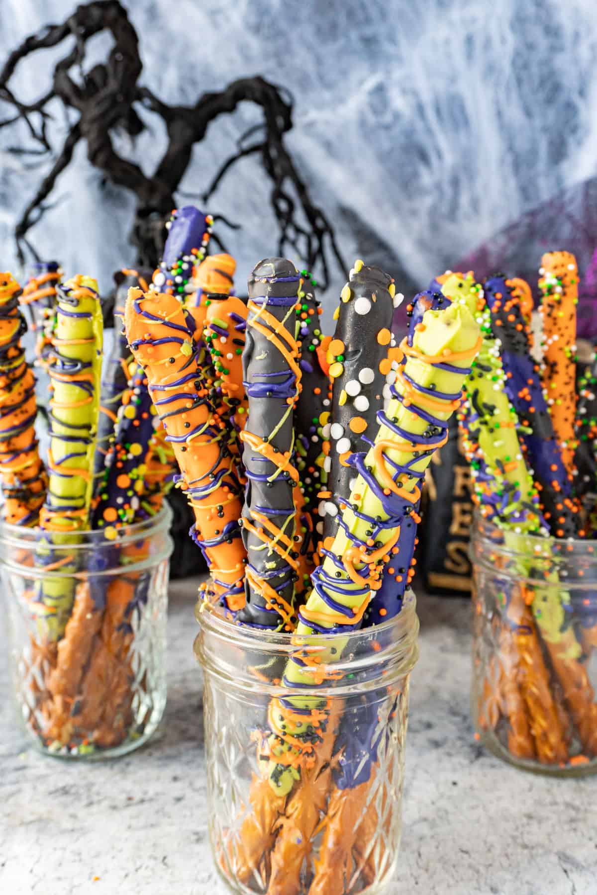 Halloween decorated pretzel rods in mason jars with Halloween decorations in the background.