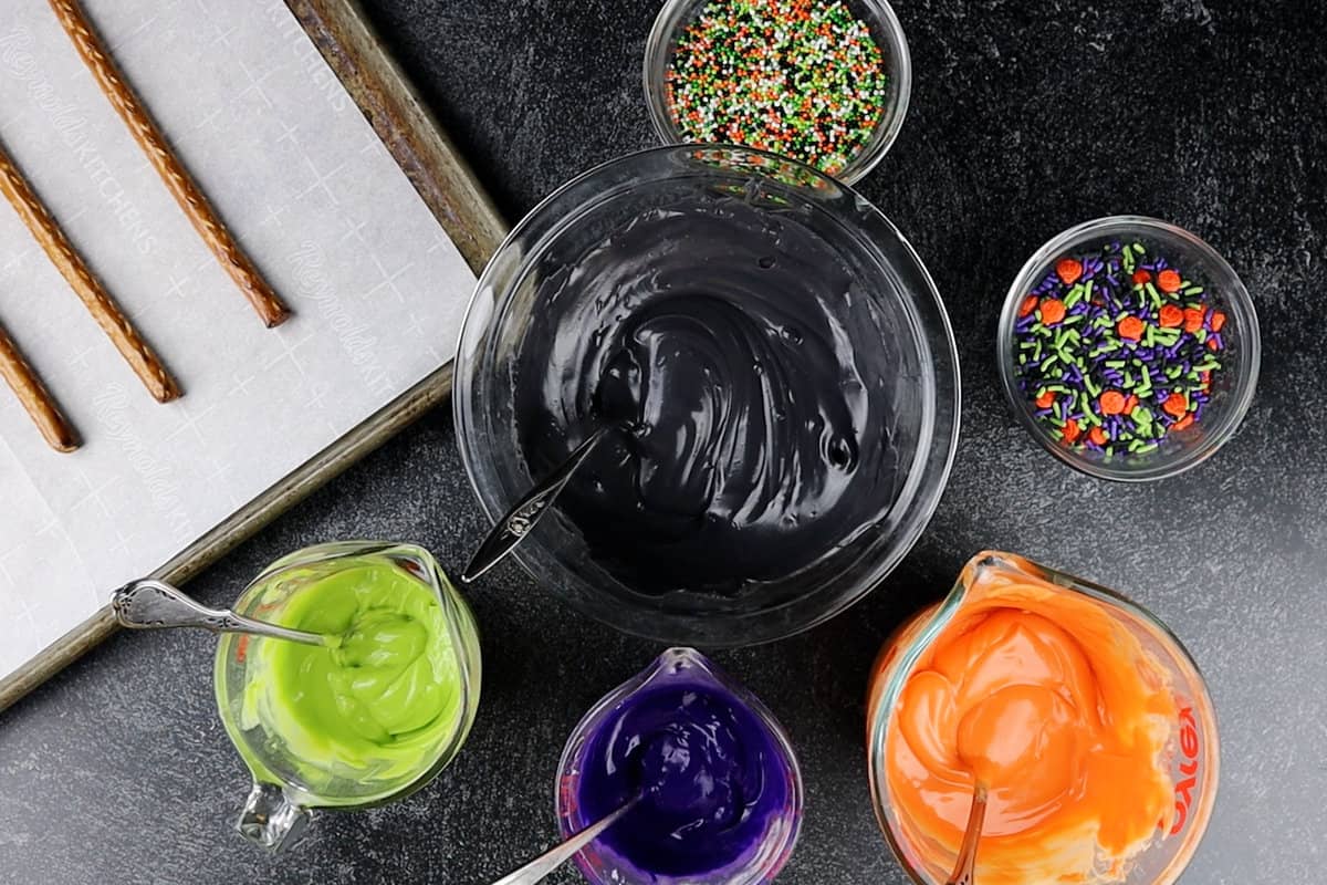 black, green, purple, and orange melted candy melts in individual bowls.