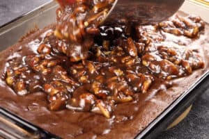 pouring pecan pie filling onto partially baked brownies