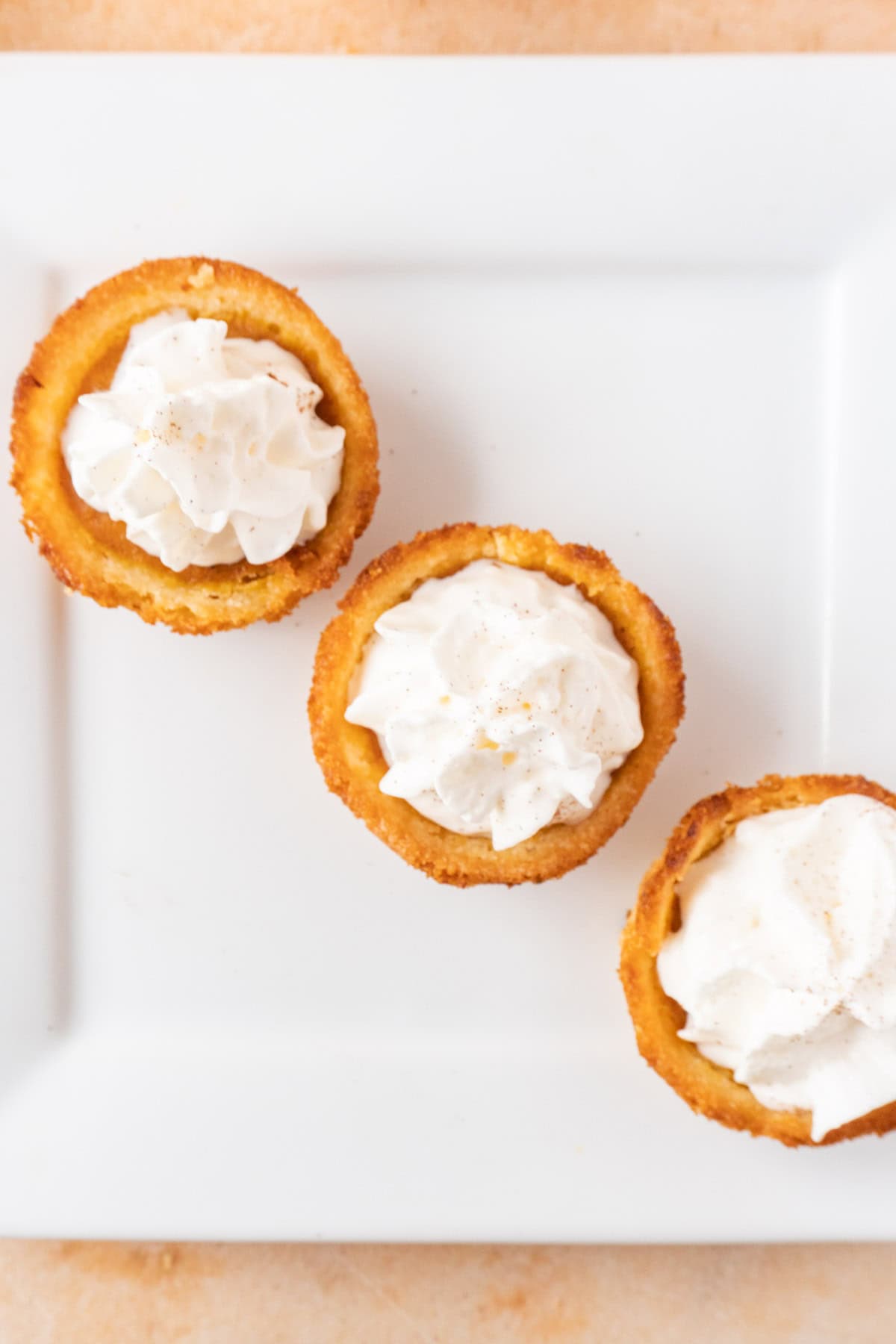 3 Pumpkin Pie cookies on a square white plate, each cookie topped with whipped cream.