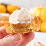 Holding a Pumpkin Pie Cookie topped with whipped cream with a bite taken out.