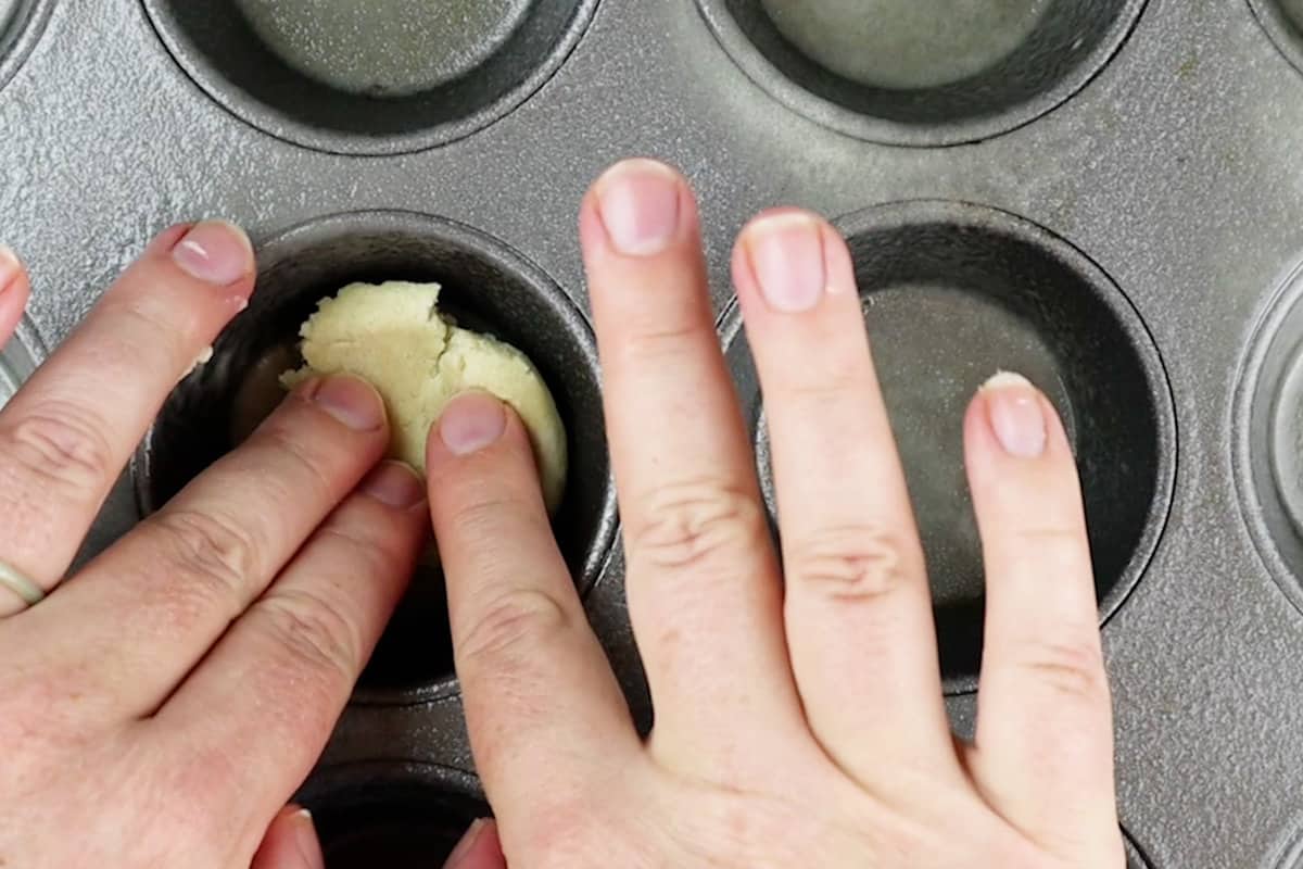 pressing sugar cookie dough into cupcake tiin