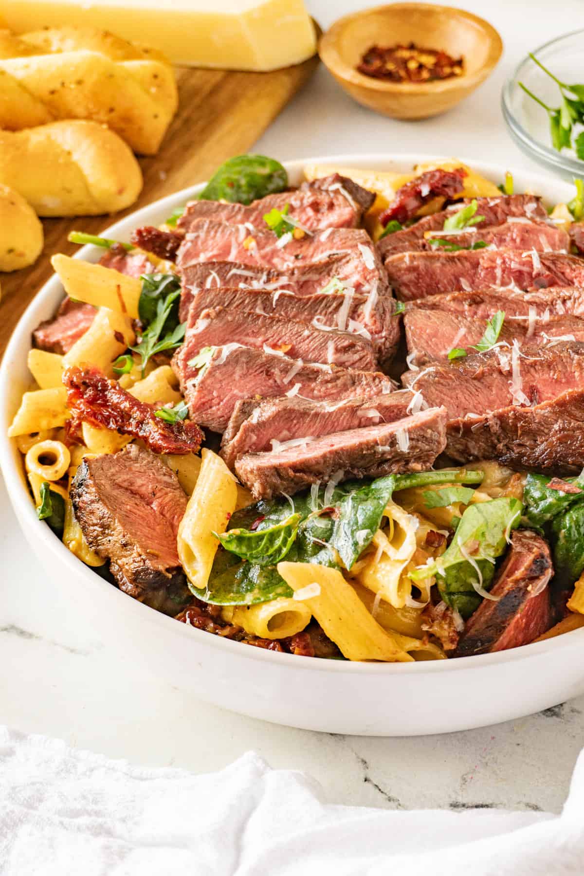 steak pasta in bowl with bread in back ground