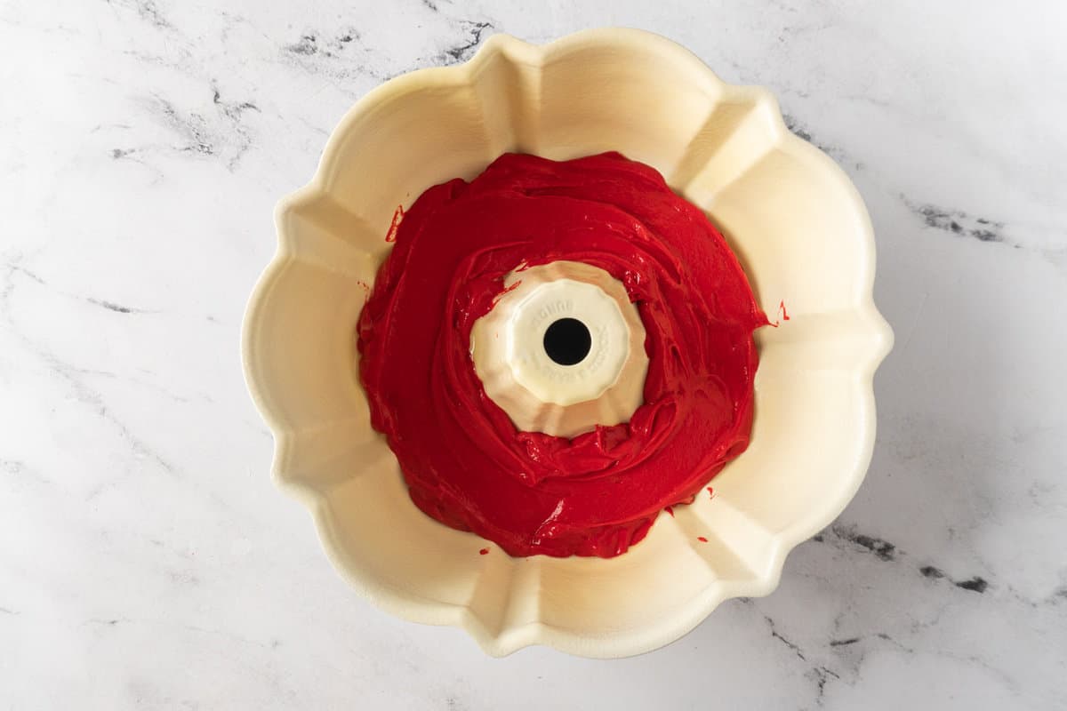 adding red cake batter to bottom of bundt pan