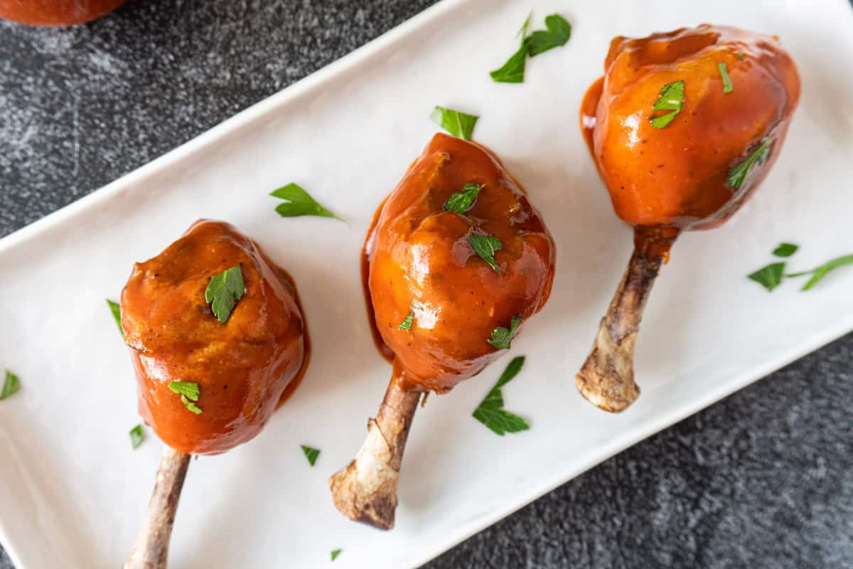 three chicken lollipops dipped in bbq sauce on platter