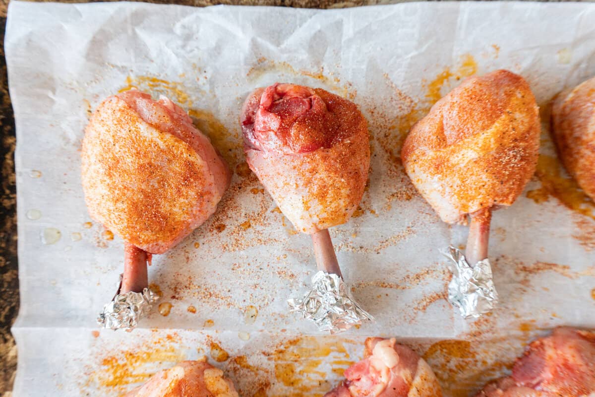 raw chicken lollipops with seasoning on baking sheet