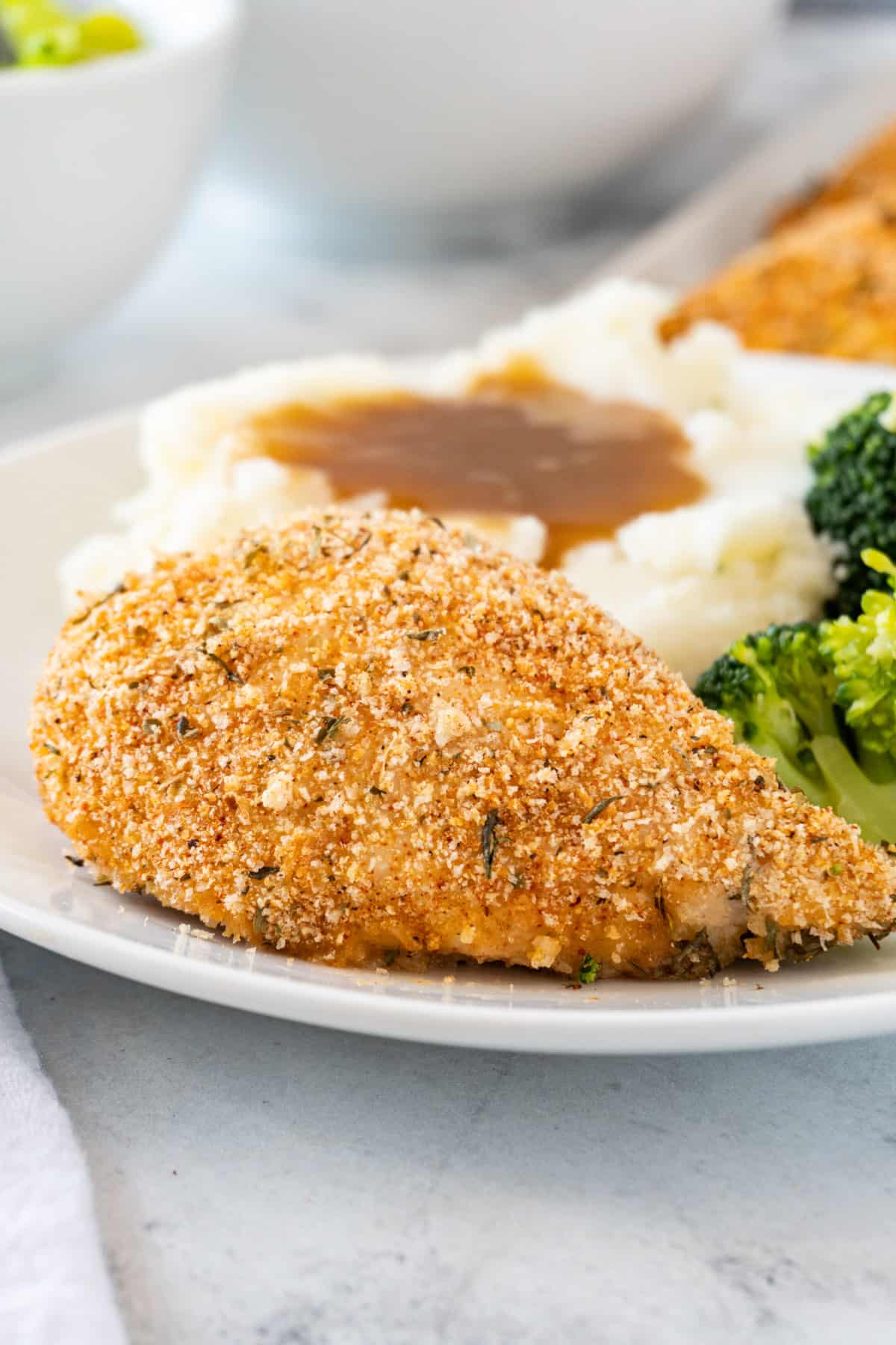 shake and bake chicken cooked next to broccoli and mashed potatoes and gravy on white plate.