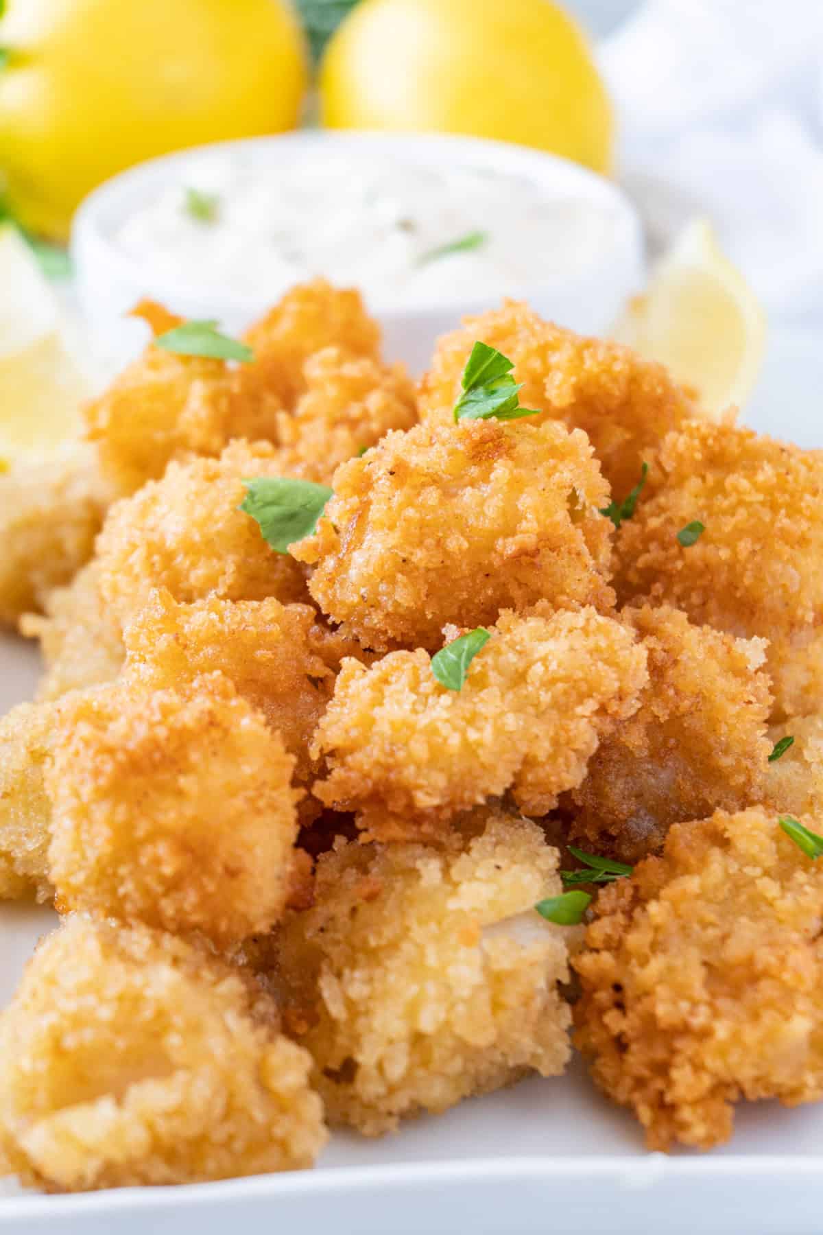 fried scallops on a white plate with tartar sauce in a white bowl near by.