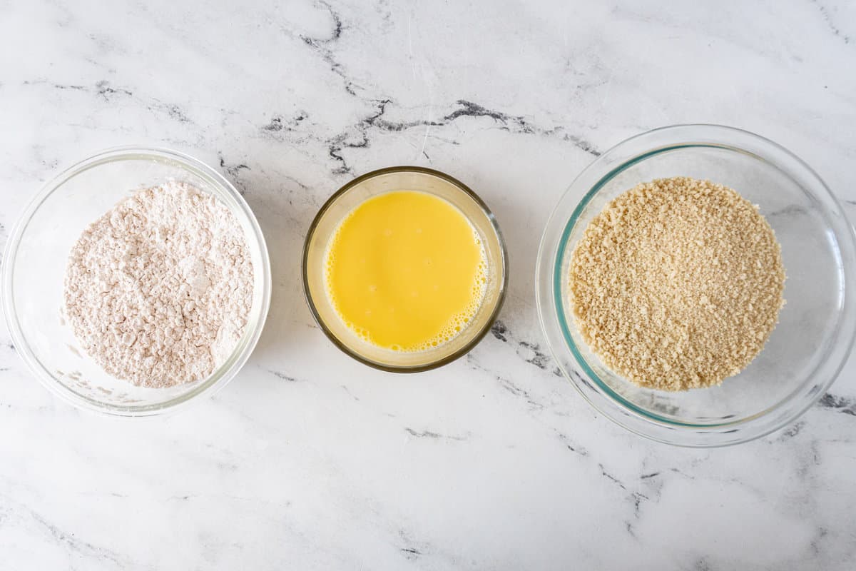 flour mixture, whisked eggs, and bread crumb mixture in bowls