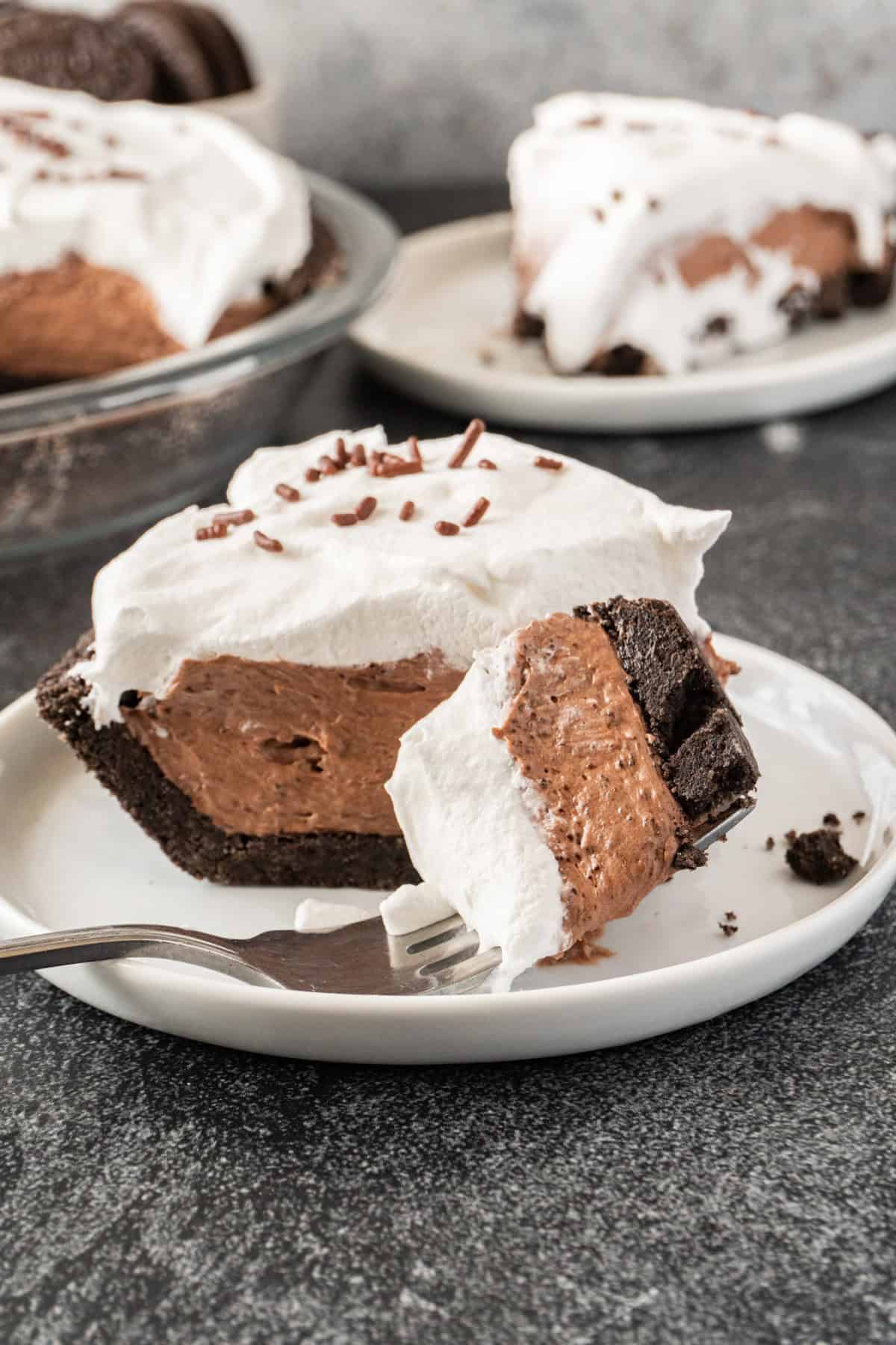 Chocolate pudding pie slice on a white plate with a bite of pie on a fork, showing the distinct layers of the pie.