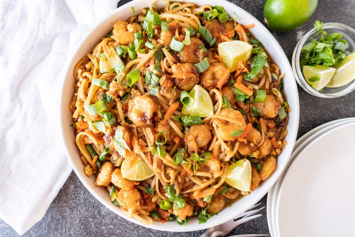 shrimp pad thai in white dish with limes and cilantro in separate bowl