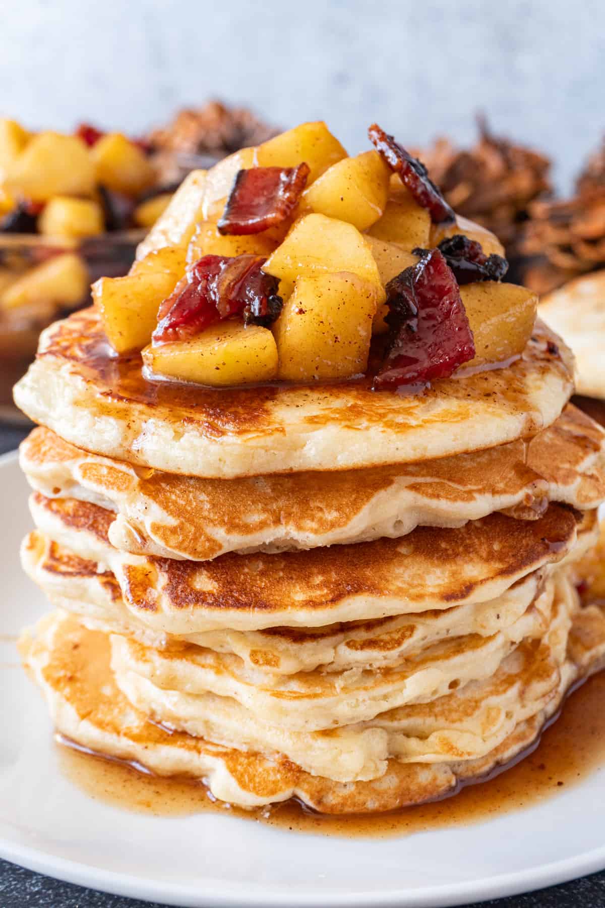 whole stack of bacon pancakes with apple topping, sitting on a white plate.