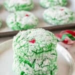 Grinch Cookies stacked 3 high on small white plate with more cookies in the background.