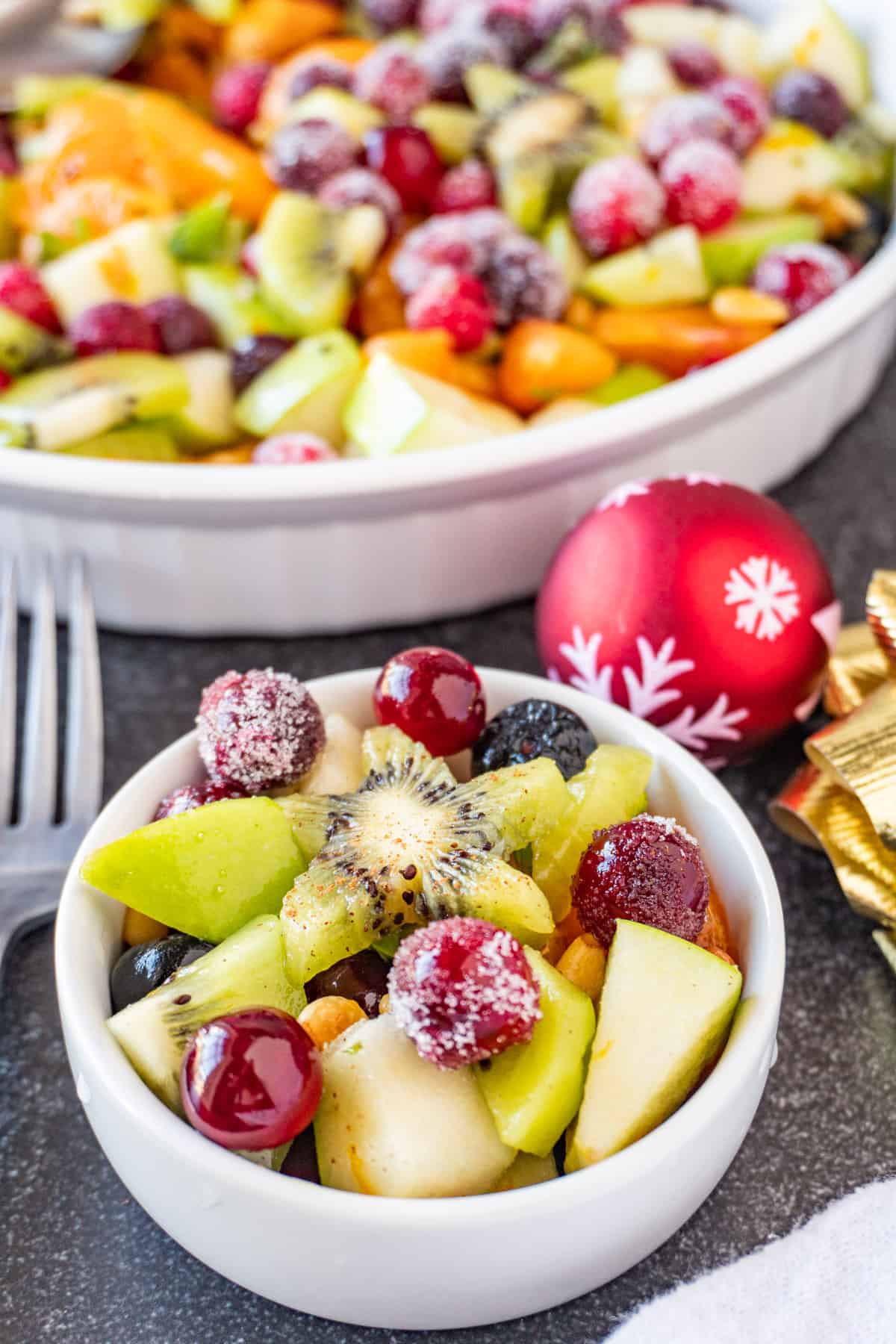 Christmas fruit salad in small white bowl, with sugar coated cranberries and a star kiwi on top.