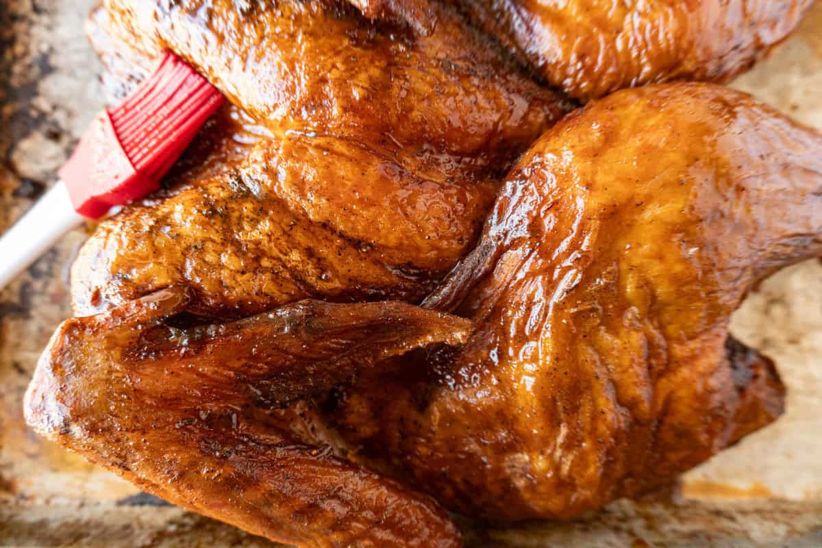 brushing glaze on turkey while it sits on a baking sheet.