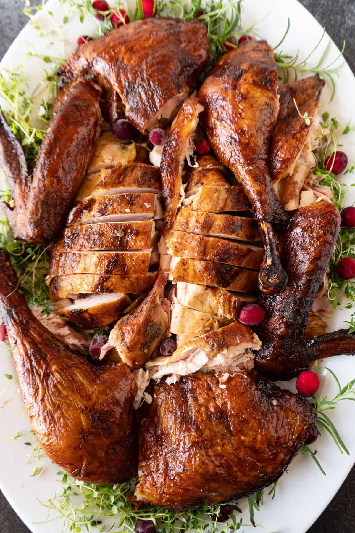 carved smoked turkey on a white platter surrounded by herbs and cranberries.