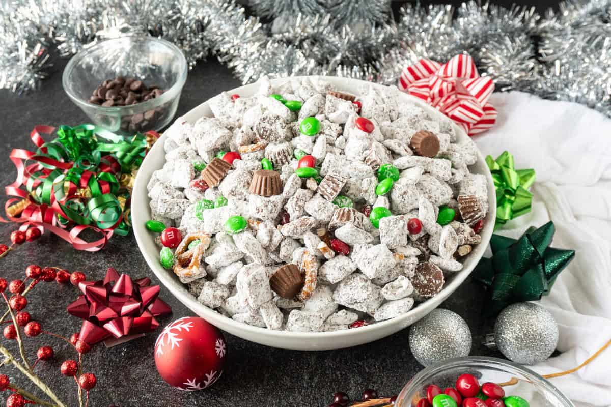 Christmas Chex mix in white bowl, surrounded by Christmas decorations.
