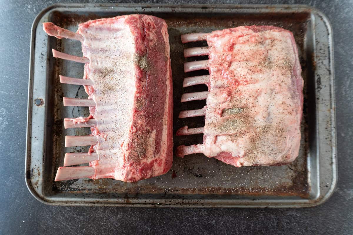uncooked racks of lamb with salt and pepper sprinkled over.