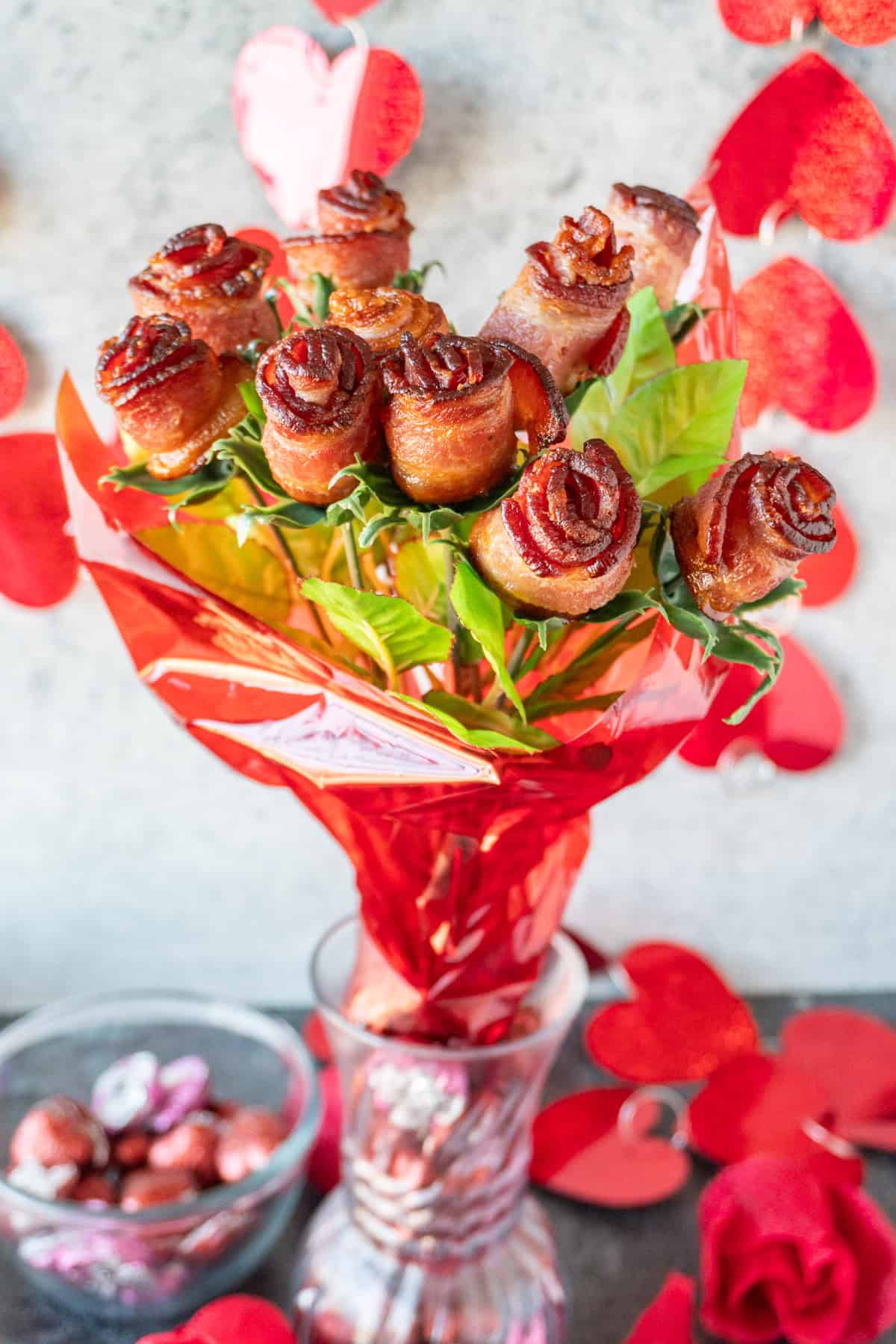 bouquet of bacon roses wraped in red cellophane and in vase filled with chocolates.